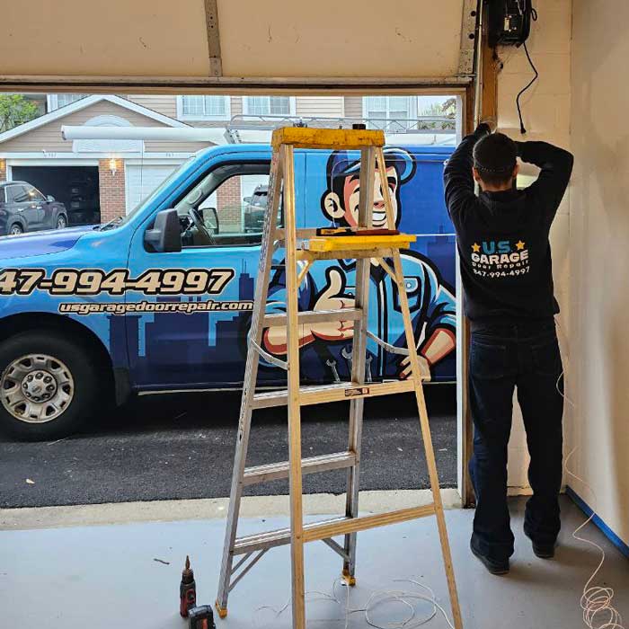 Technician working beside a garage door with a US Garage Door Repair service van outside